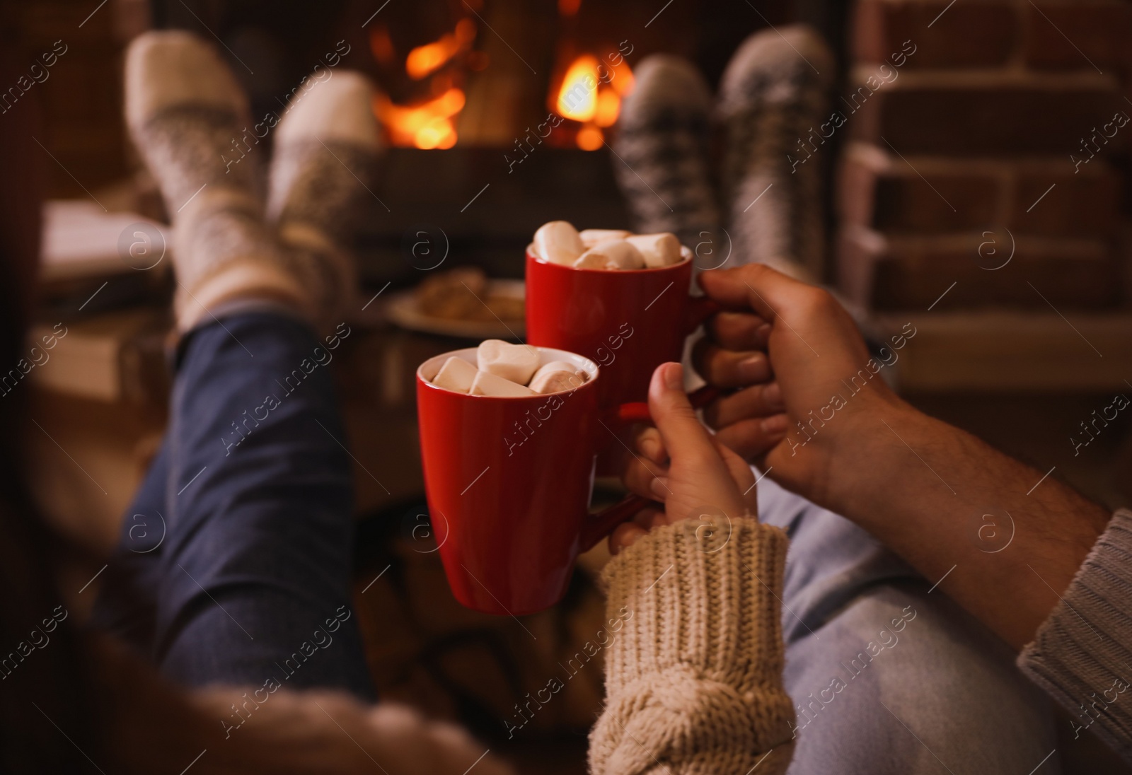 Photo of Lovely couple with sweet cocoa near fireplace indoors, closeup