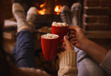Photo of Lovely couple with sweet cocoa near fireplace indoors, closeup