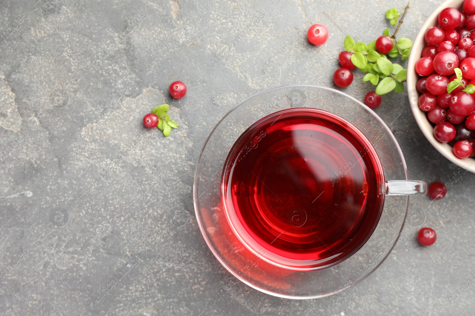 Photo of Tasty hot cranberry tea in glass cup and fresh berries on light grey textured table