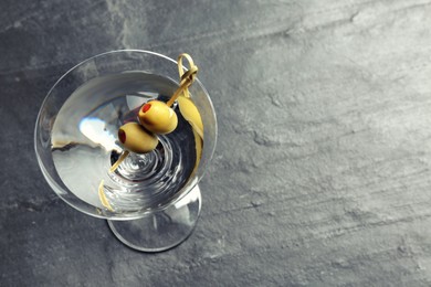 Photo of Martini cocktail with olives on grey table, above view. Space for text