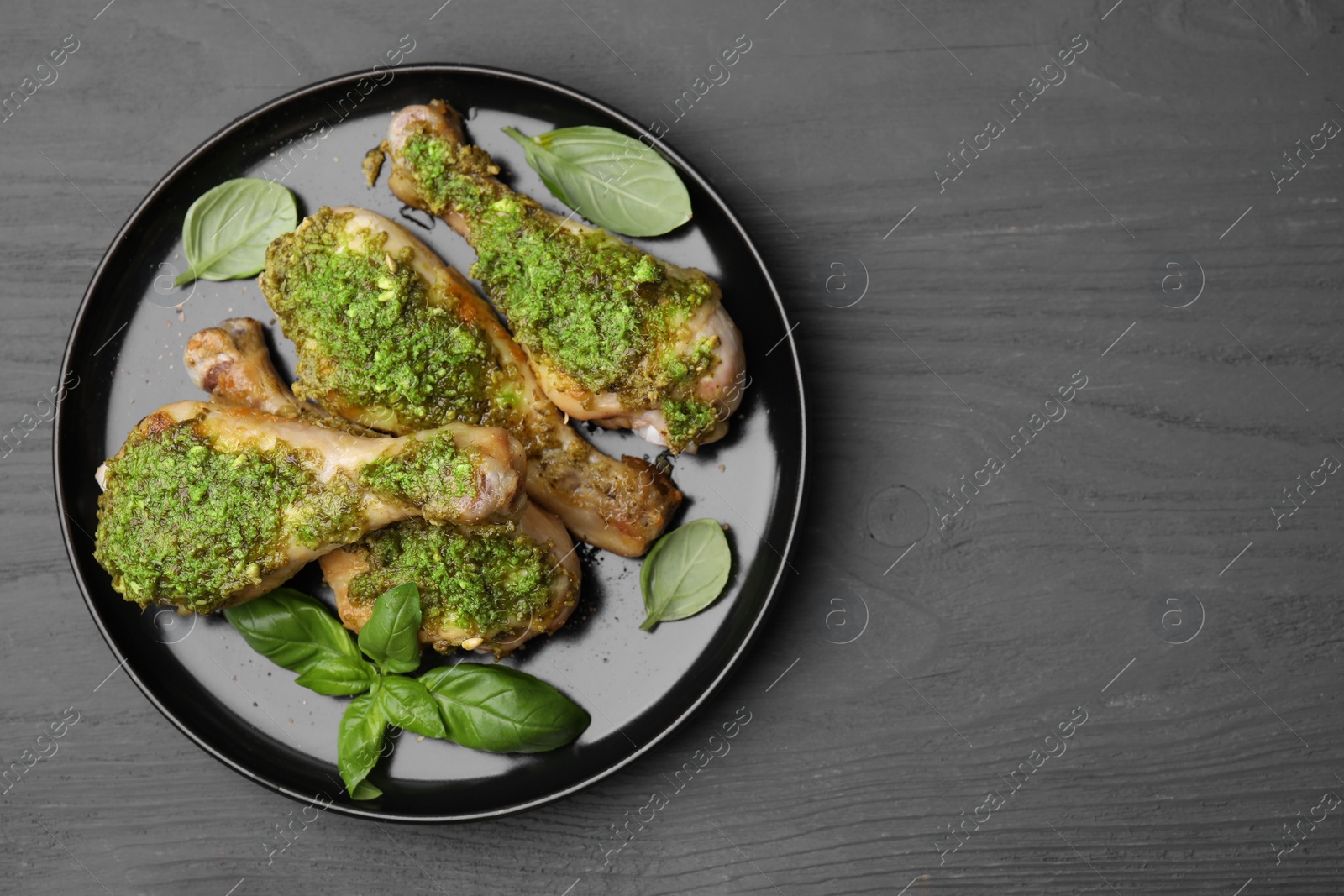 Photo of Delicious fried chicken drumsticks with pesto sauce and basil on gray wooden table, top view. Space for text