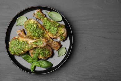 Delicious fried chicken drumsticks with pesto sauce and basil on gray wooden table, top view. Space for text