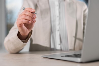 Woman with pen working on laptop at wooden table, closeup. Electronic document management