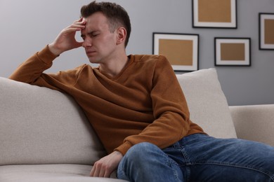 Photo of Sad man suffering from headache on sofa indoors