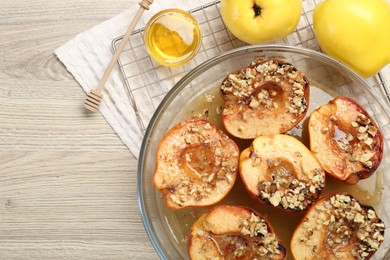 Delicious baked quinces with nuts in bowl, honey and fresh fruits on wooden table, flat lay. Space for text