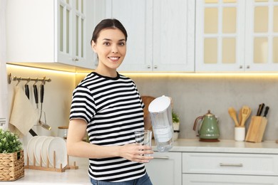 Woman with glass of water and filter jug in kitchen