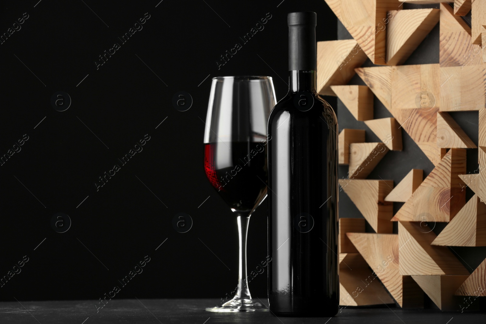 Photo of Stylish presentation of red wine in bottle and wineglass on table against black background, space for text