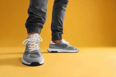 Man wearing stylish sneakers on yellow background, closeup. Space for text