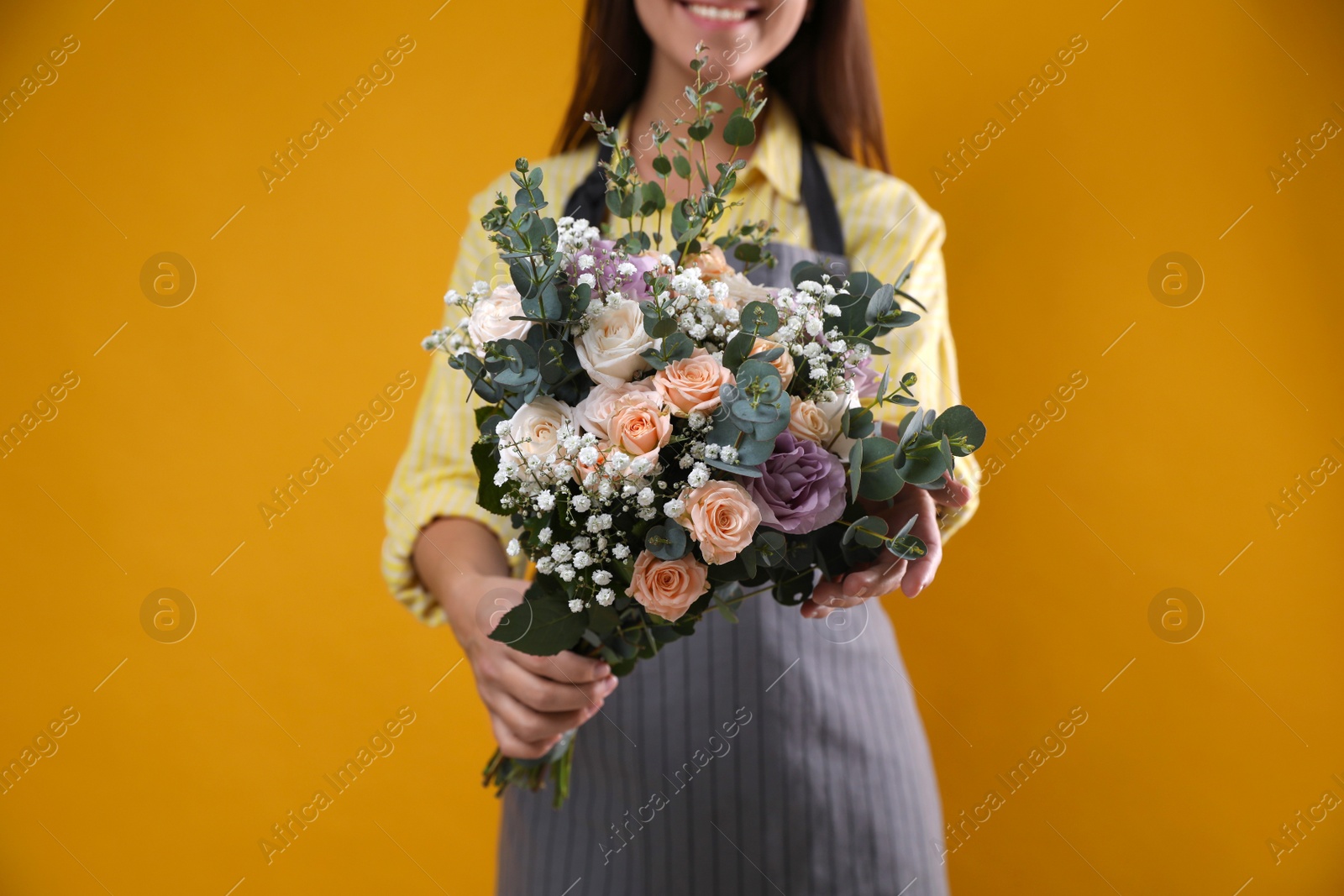 Photo of Florist holding beautiful wedding bouquet on yellow background, closeup