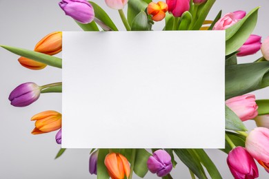 Blank birthday card on beautiful tulip flowers against grey background, flat lay. Space for text