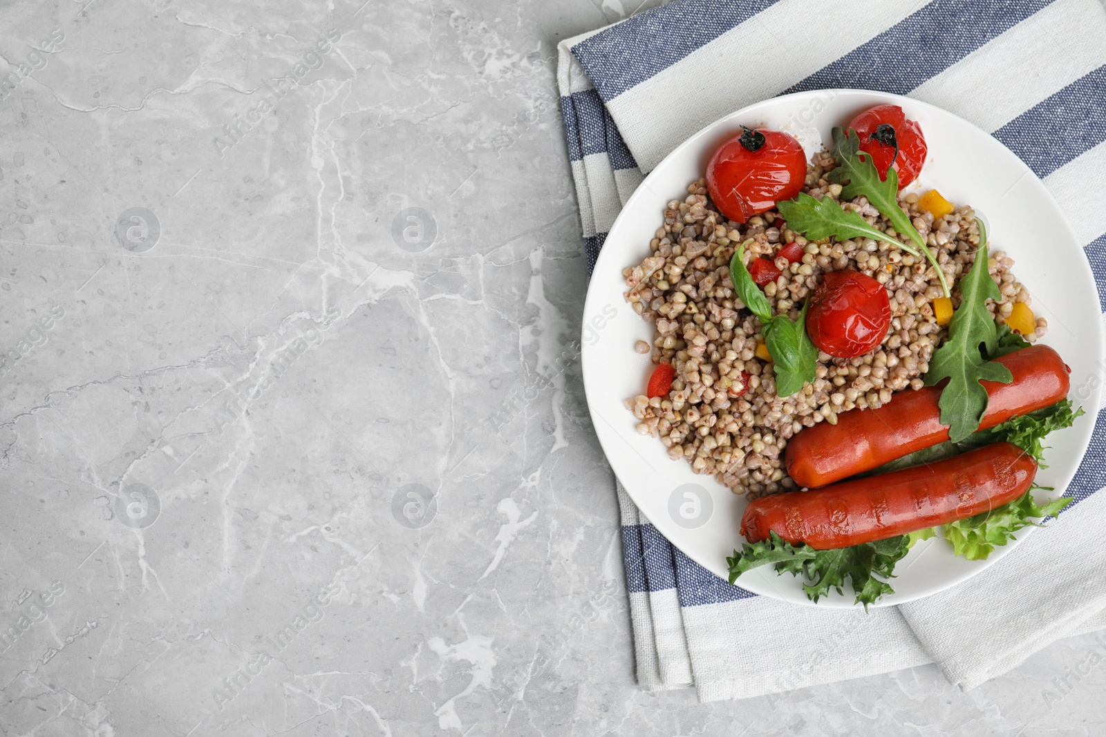 Photo of Tasty buckwheat porridge with sausages on light grey marble table, flat lay. Space for text