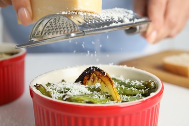 Photo of Woman grating cheese onto baked green beans at table, closeup