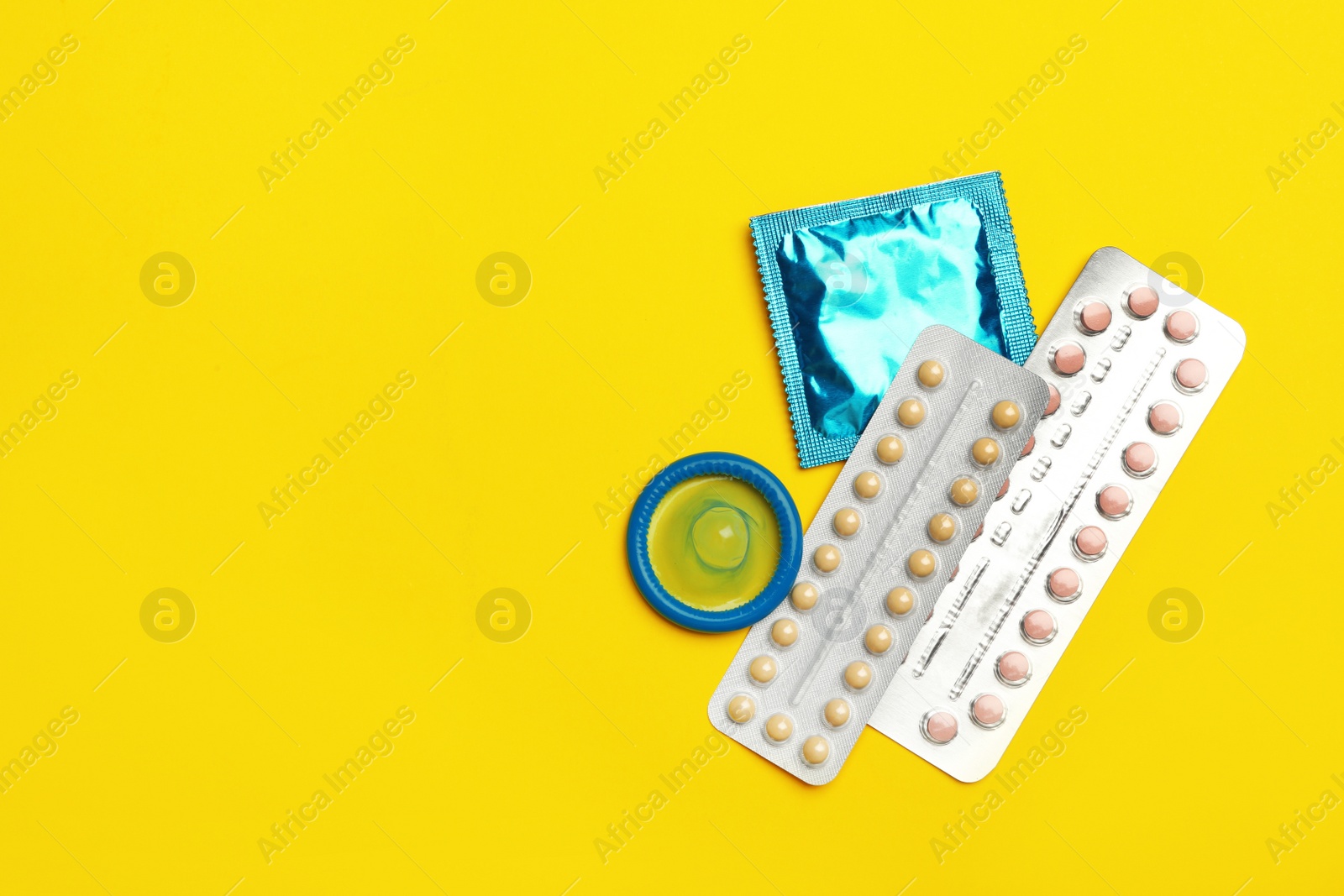 Photo of Condoms and birth control pills on yellow background, flat lay with space for text. Safe sex concept