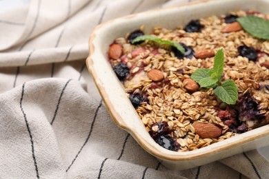 Photo of Tasty baked oatmeal with berries and almonds in baking tray on tablecloth, closeup. Space for text