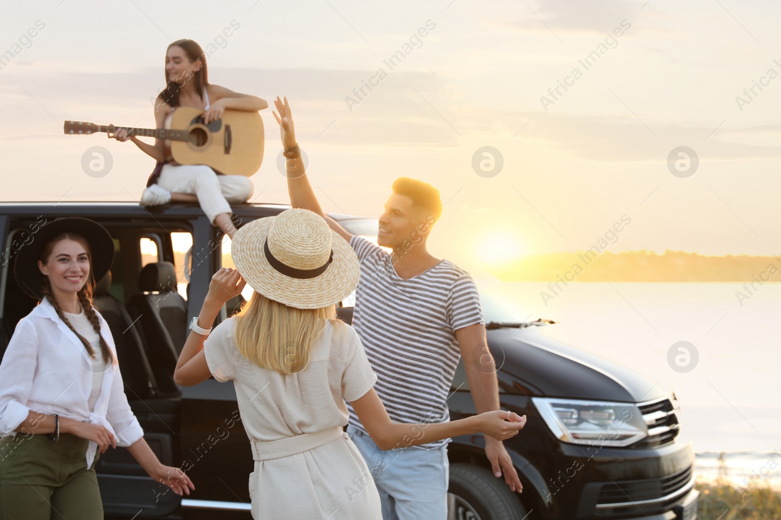 Photo of Happy friends having fun near car outdoors at sunset. Summer trip