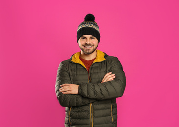 Happy young man in warm clothes on pink background. Winter vacation