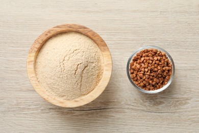 Photo of Buckwheat flour and grains in bowls on white wooden table, top view