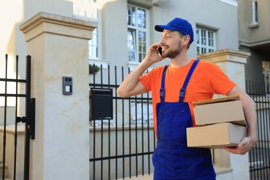 Photo of Courier with parcels talking on smartphone outdoors, space for text. Order delivery