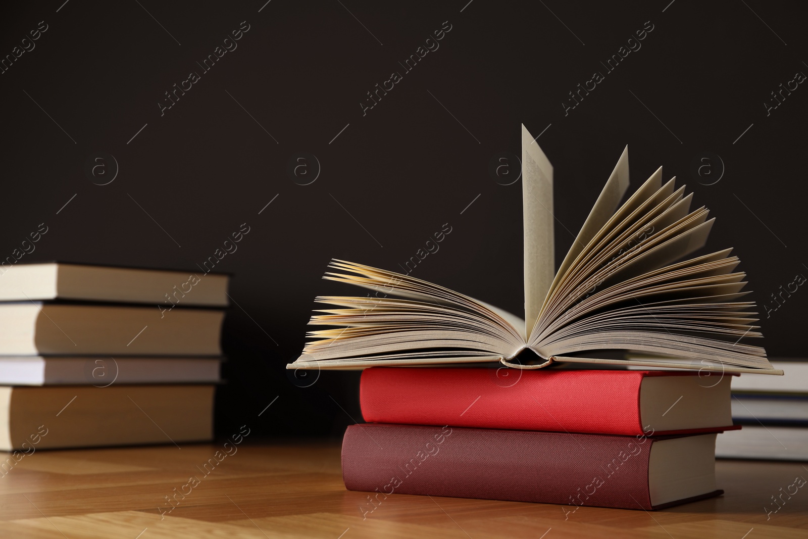 Photo of Many books stacked on wooden table near black wall, space for text