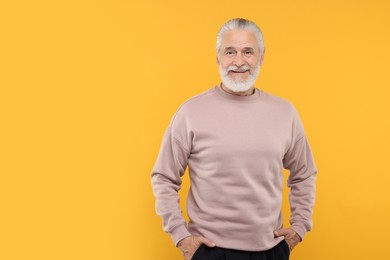 Portrait of handsome senior man on orange background. Space for text