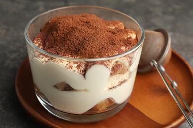 Photo of Delicious tiramisu in glass and sieve with cocoa powder on grey table, closeup