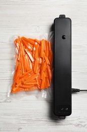 Photo of Vacuum packing sealer and plastic bag with cut carrots on white wooden table, top view