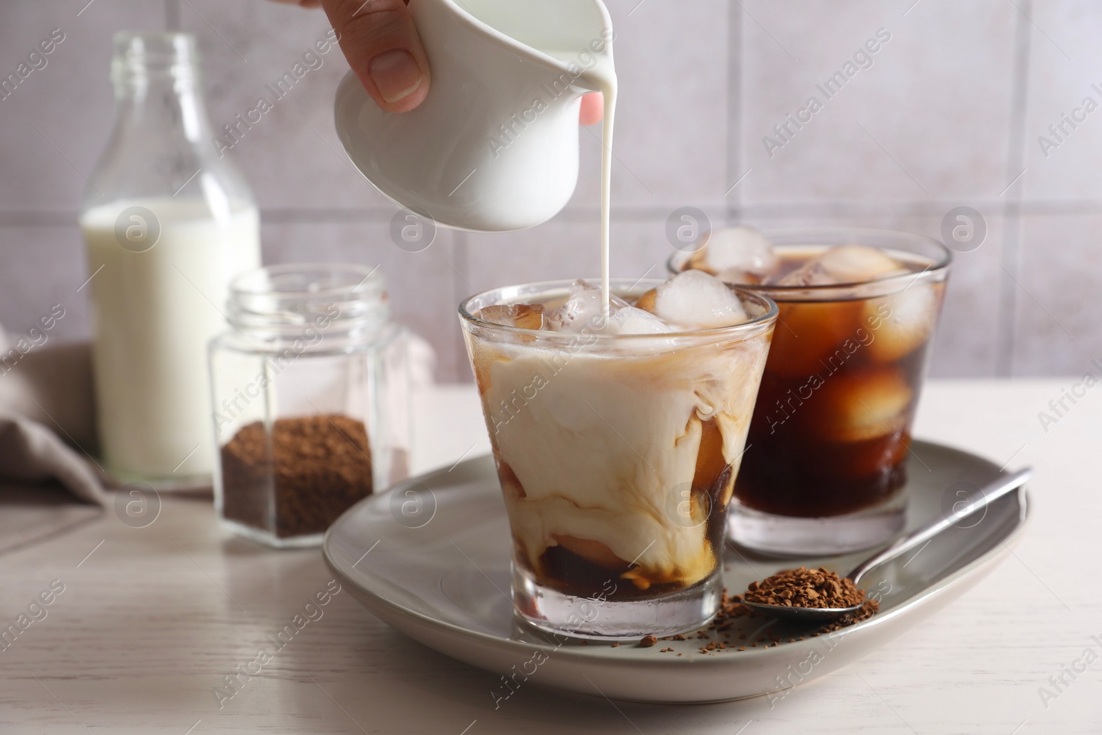 Photo of Woman pouring milk into glass with refreshing iced coffee at light table, closeup