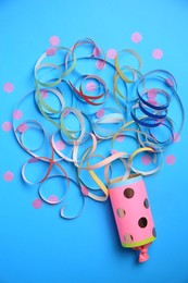 Photo of Beautiful serpentine and confetti bursting out of party popper on light blue background, flat lay