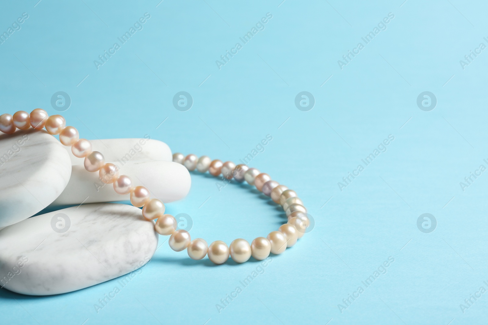 Photo of White marble stones with elegant jewelry on light blue background. Space for text