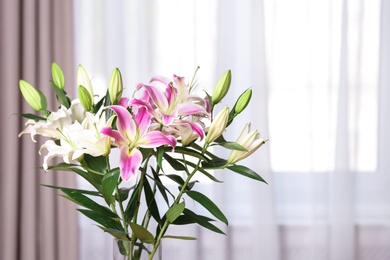 Photo of Vase with bouquet of beautiful lilies on blurred background. Space for text