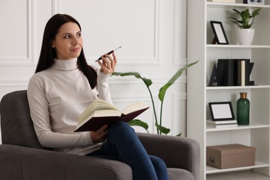 Photo of Woman using cigarette holder for smoking while reading book indoors