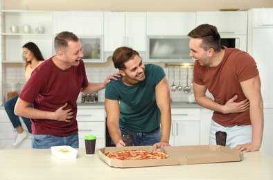 Group of friends with tasty food laughing together in kitchen