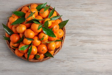 Photo of Fresh ripe juicy tangerines and green leaves on white wooden table, top view. Space for text