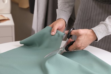 Photo of Tailor cutting fabric with scissors at table in atelier, closeup