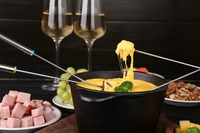 Photo of Dipping different products into fondue pot with melted cheese on table, closeup