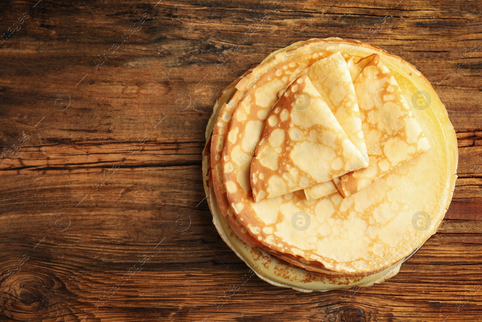 Photo of Stack of fresh thin pancakes on wooden table, top view. Space for text