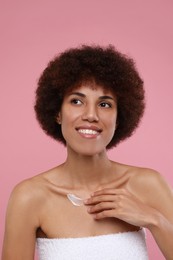 Photo of Beautiful young woman applying cream onto body on pink background