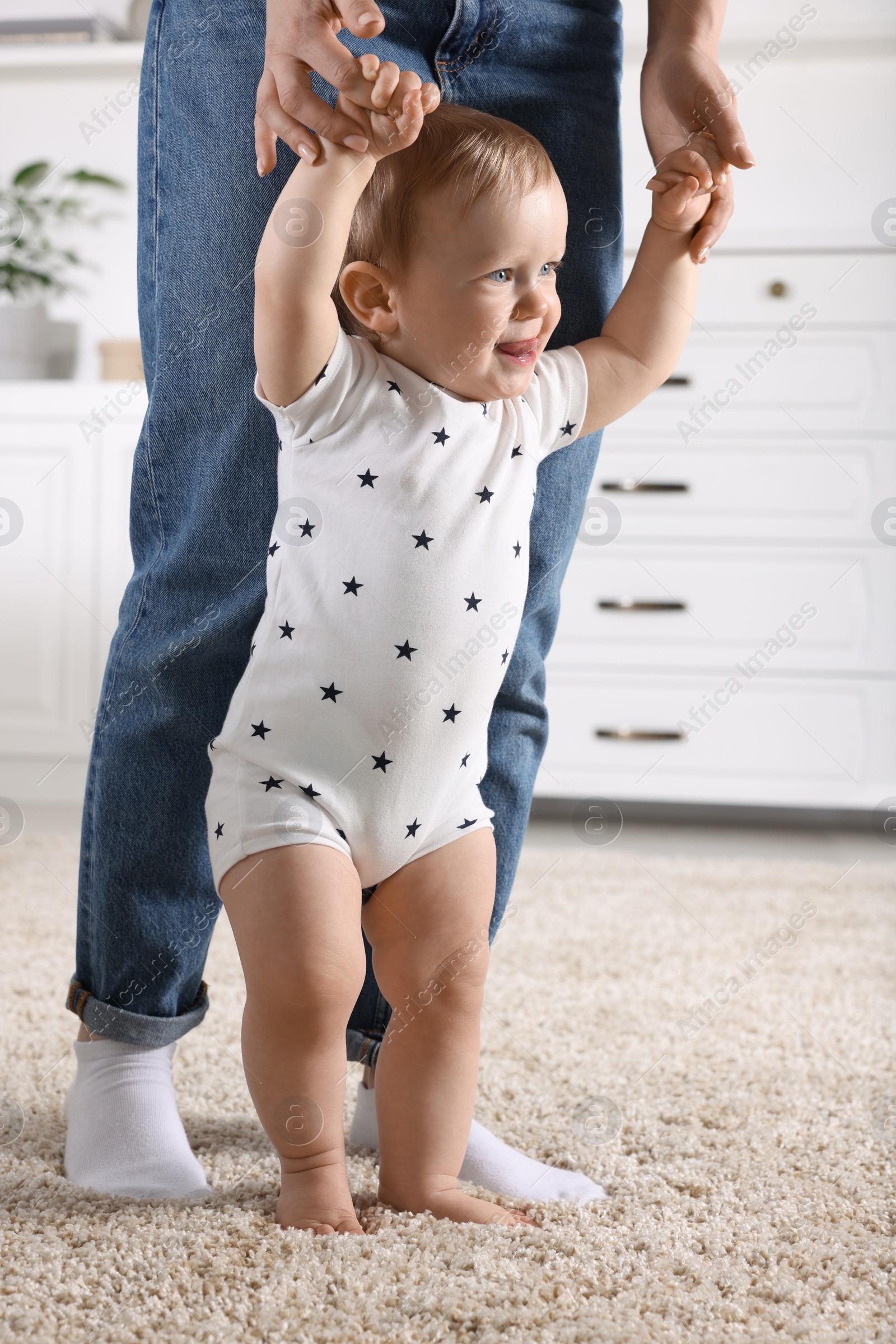 Photo of Mother supporting her baby son while he learning to walk on carpet at home