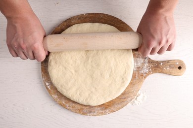 Photo of Man rolling dough with wooden pin at white table, top view