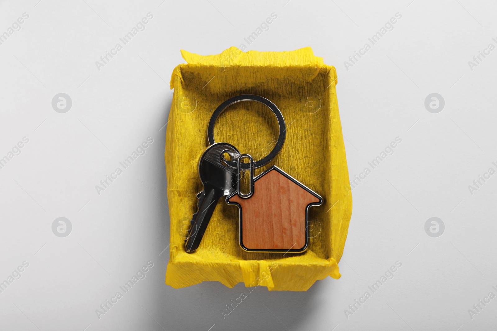 Photo of Key with trinket in shape of house and gift box on light grey background, top view. Housewarming party