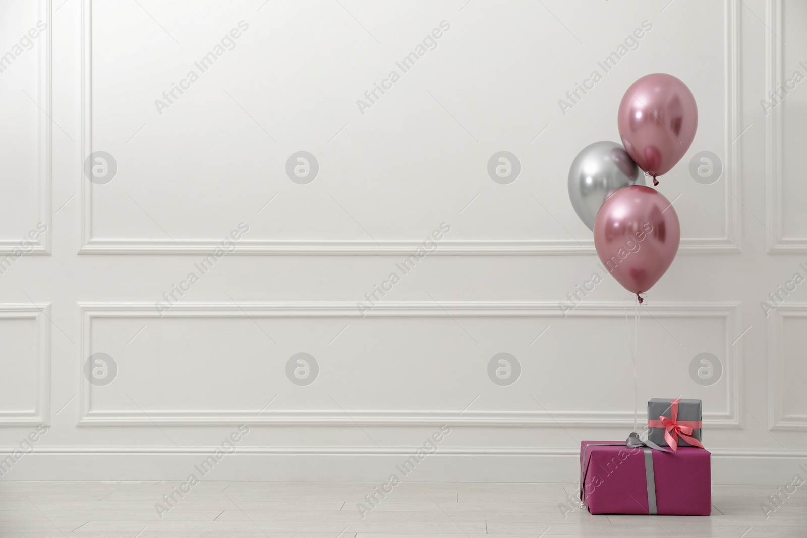 Photo of Gift boxes and balloons near white wall. Space for text