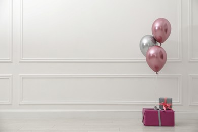 Gift boxes and balloons near white wall. Space for text