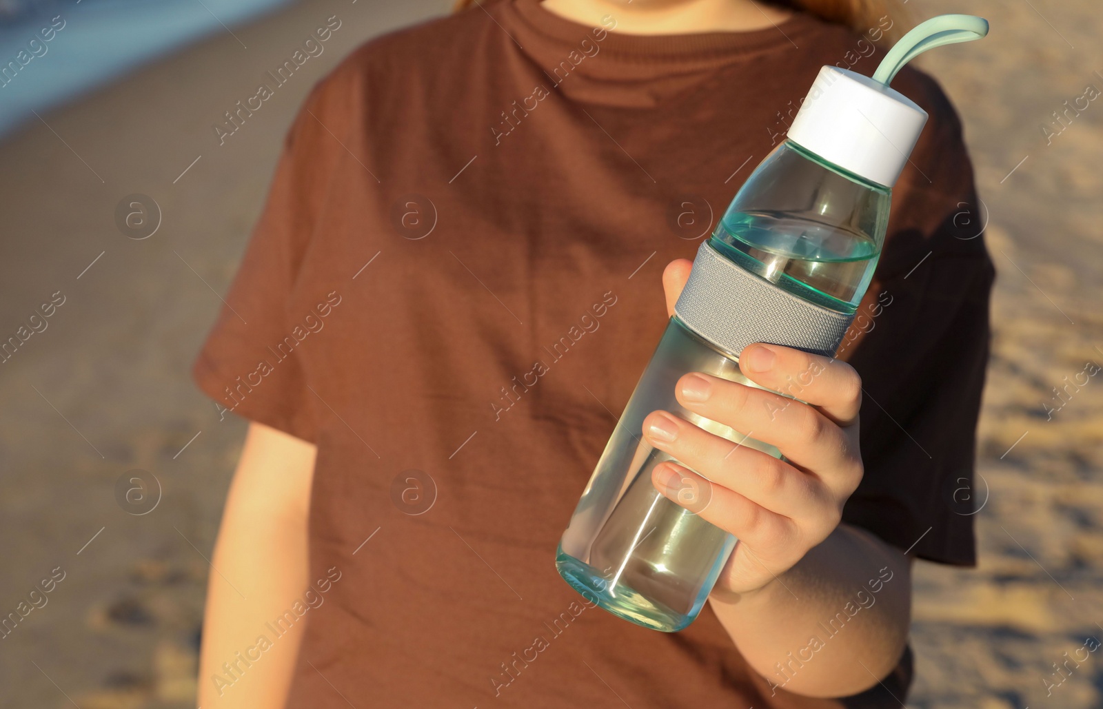 Photo of Woman holding glass bottle with water near sea, closeup