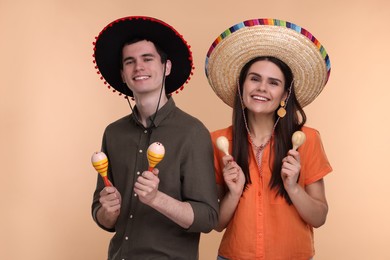 Photo of Lovely couple woman in Mexican sombrero hats with maracas on beige background