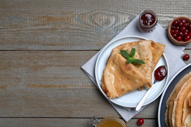 Photo of Delicious crepes served with mint, cranberries and jam on grey wooden table, flat lay. Space for text