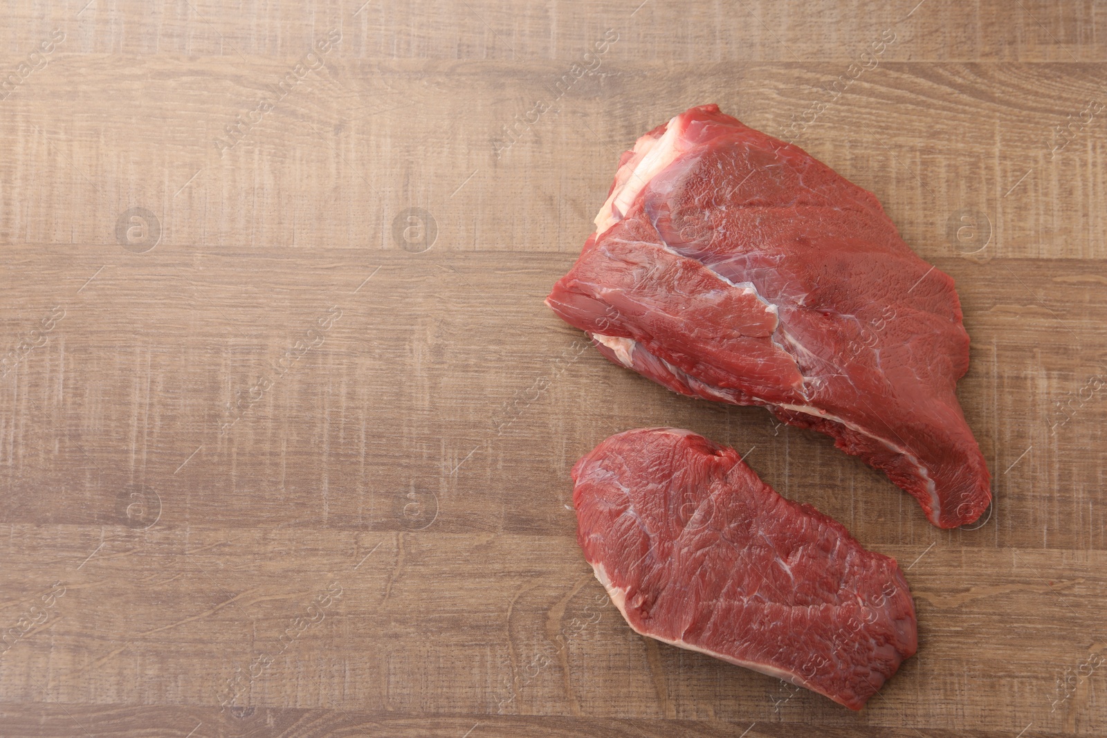 Photo of Pieces of raw beef meat on wooden table, flat lay. Space for text