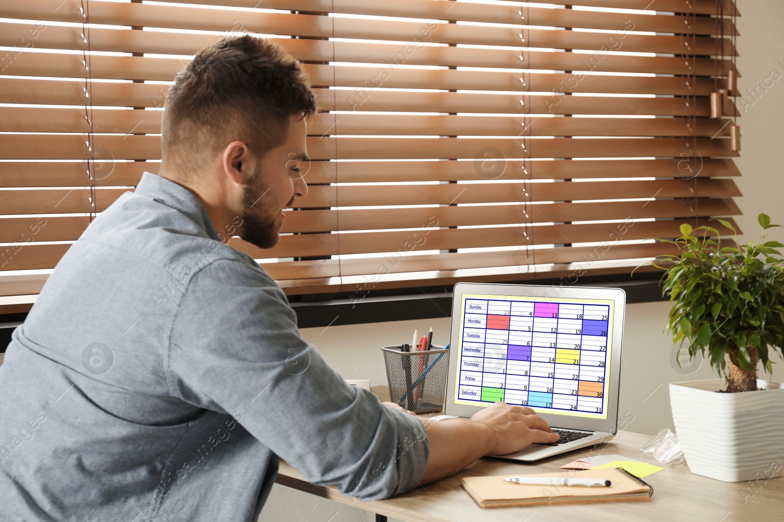 Photo of Young man using calendar app on laptop in office