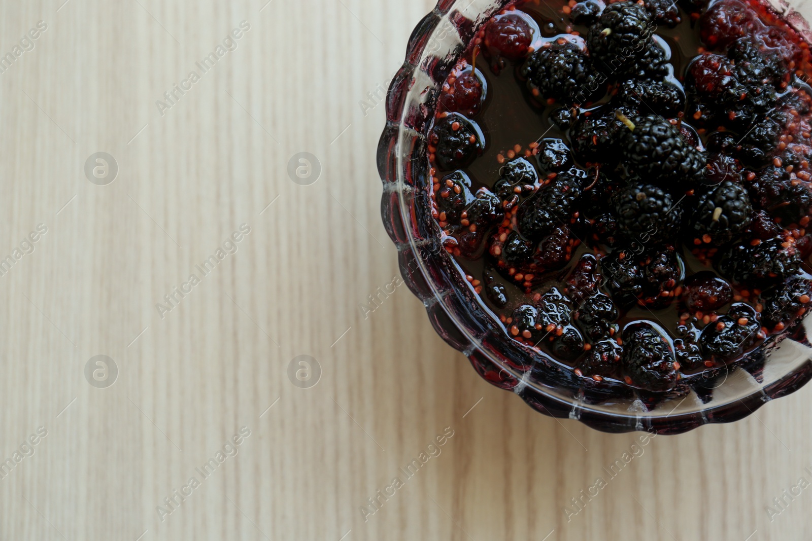Photo of Bowl of sweet black mulberry jam on wooden table, top view. Space for text