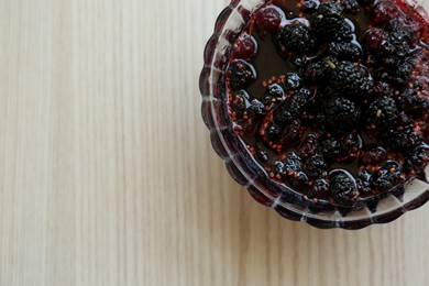 Bowl of sweet black mulberry jam on wooden table, top view. Space for text