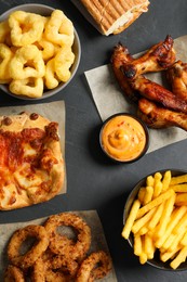 French fries, onion rings and other fast food on black table, flat lay